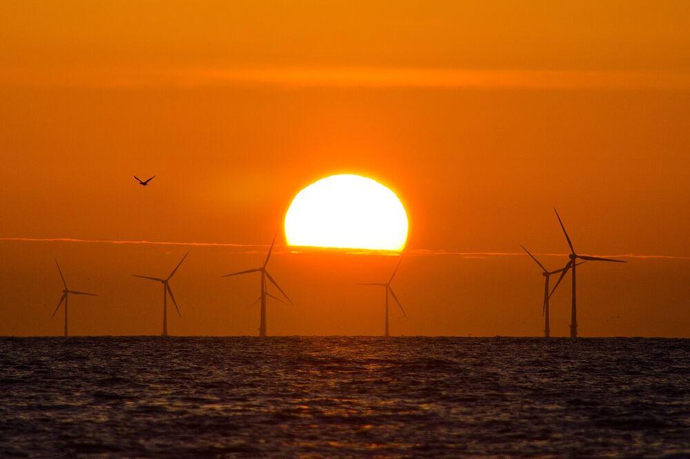 Zon zakt in de Noordzee bij Castricum aan Zee, met windturbines op de horizon